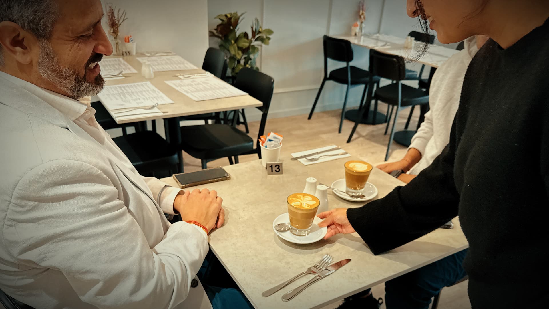 Staff member serving two lattes with flower latte art to a smiling customer at No9 The Cafe.