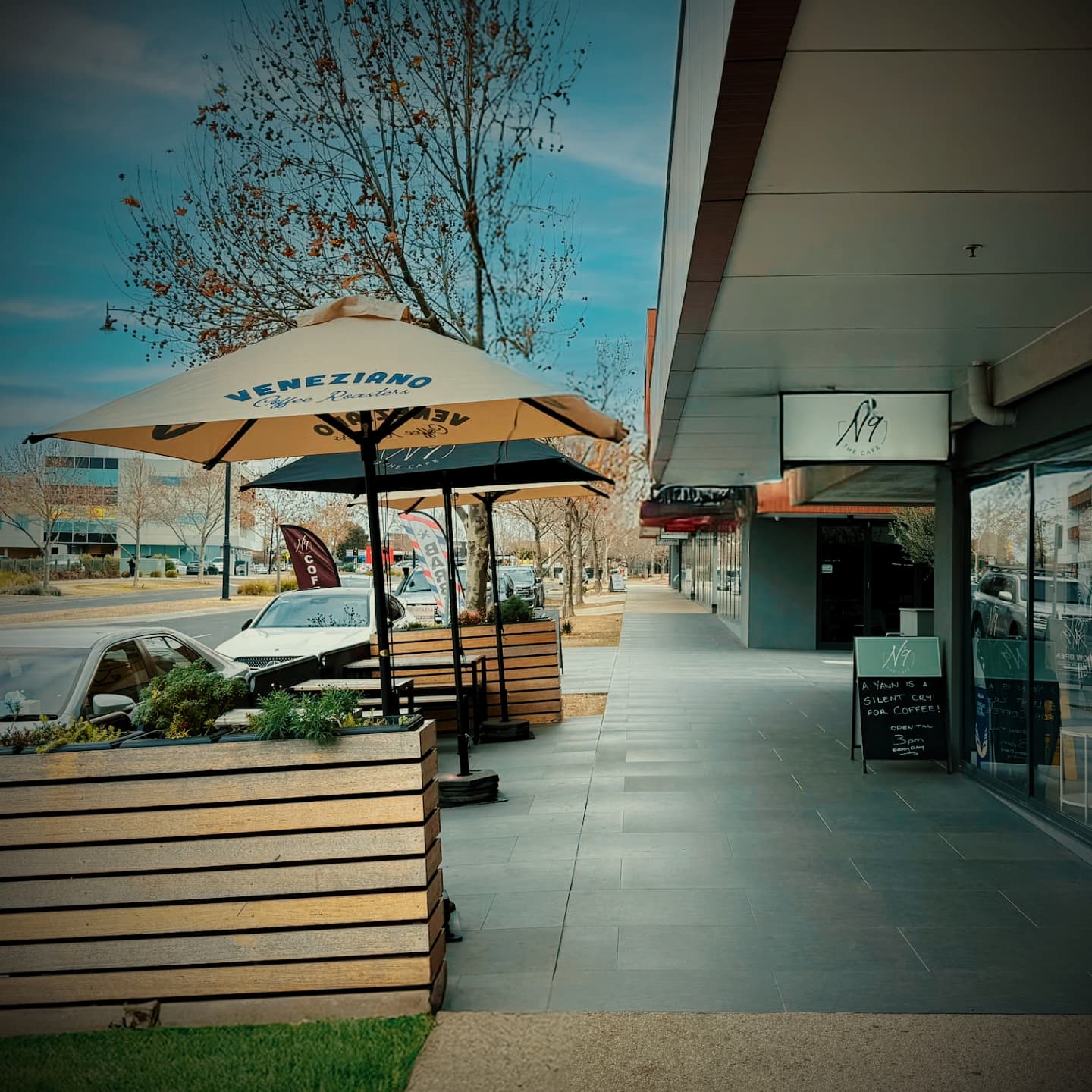 No9 The Cafe shopfront in Caroline Springs with outdoor seating, umbrellas, timber planters and a chalkboard sign.